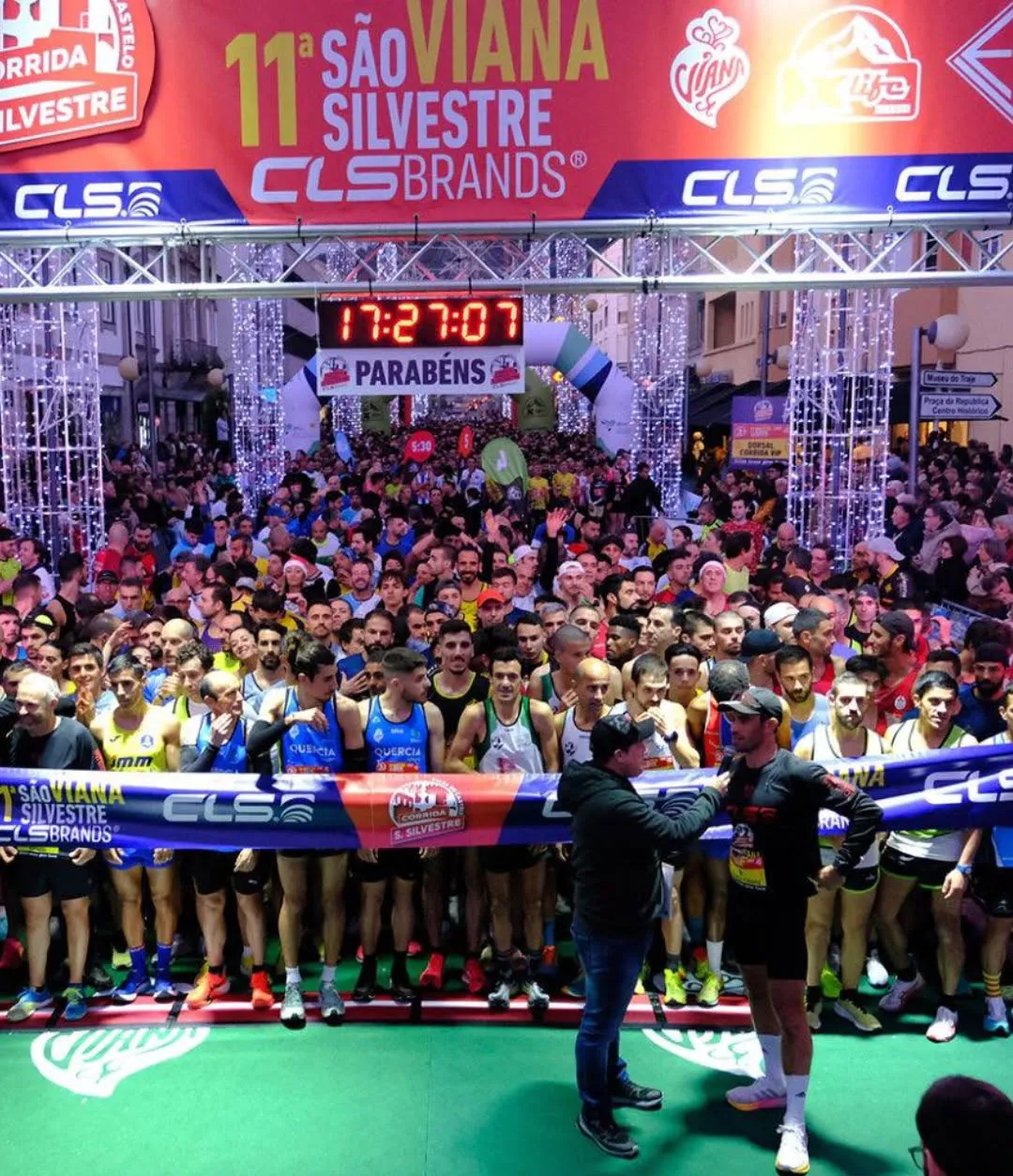 Multidão de corredores à partida da Corrida São Silvestre em Viana do Castelo, sob pórtico iluminado com a marca CLS Brands.